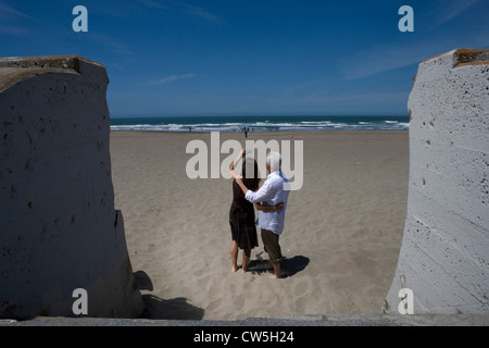 Vue arrière d'un couple mature pour prendre des photos avec un appareil photo numérique sur la plage Banque D'Images