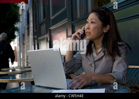Businesswoman assis devant un ordinateur portable et de parler sur un téléphone mobile Banque D'Images