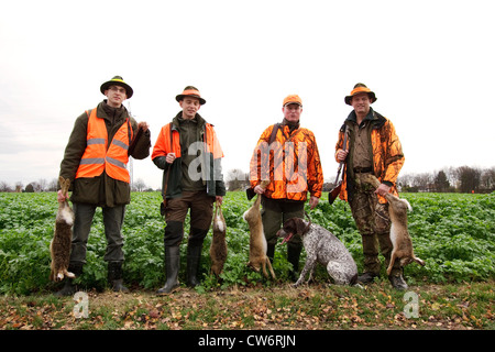 Lièvre d'Europe (Lepus europaeus), quatre tireurs d'une battue debout à la lisière d'un champ avec leur proie dans les mains de quatre lièvres, Allemagne Banque D'Images