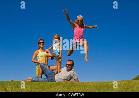 Jeune famille avec deux petites filles posant sur une pelouse en face d'un ciel bleu, France Banque D'Images