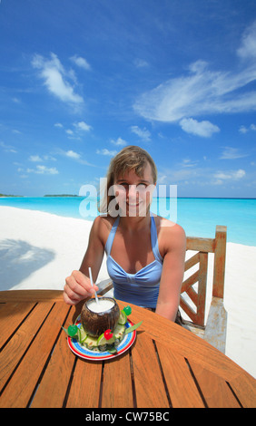 Jeune femme assise dans un bar à la plage, sirotant un cocktail Banque D'Images