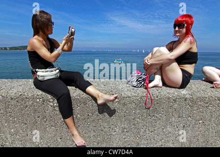 Deux jeunes femme assise sur quai, prendre des photos de l'autre, l'Allemagne, Schleswig-Holstein, Luebeck, Travemuende Banque D'Images