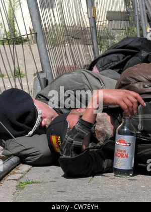 Ivre sans-abri dormir à la pleine lumière sur le trottoir à côté d'une bouteille de l'alcool à haute à la Reeperbahn (red light district), l'Allemagne, St Pauli, Hambourg Banque D'Images