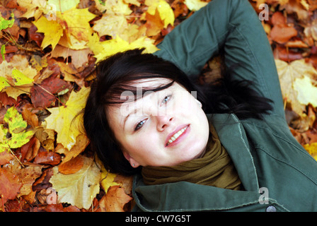 Belle fille en position couchée, allongée sur le feuillage d'automne Banque D'Images