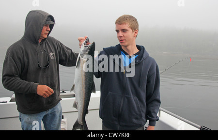 Un jeune homme est titulaire d'un saumon d'argent sur un bateau de pêche de l'Alaska. Banque D'Images