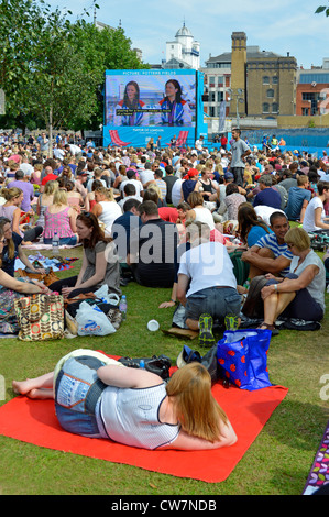 Une foule de gens s'assoient sur l'herbe pour regarder les Jeux olympiques de Londres 2012 Événement de sport de télévision grand écran de télévision en plein air dans Potters Fields Park Southwark Angleterre Royaume-Uni Banque D'Images