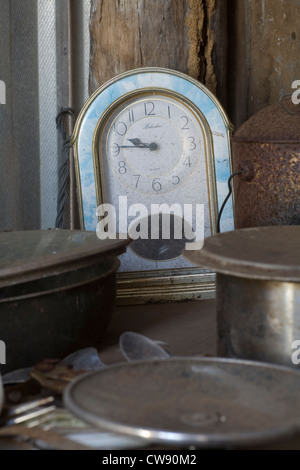 Vieux réveil gelé dans le temps dans une cabane à l'abandon parmi les ustensiles de cuisine. Banque D'Images