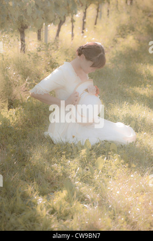 Une femme dans une robe victorienne blanche assise sur l'herbe entre les vignes Banque D'Images