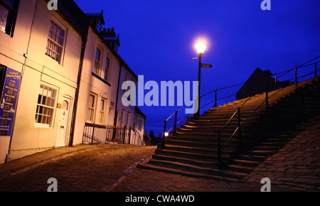 Un streetlight illumine une rue pavée et les marches de pierre qui mènent à l'abbaye de Whitby, Whitby, North Yorkshire, UK - soir Banque D'Images