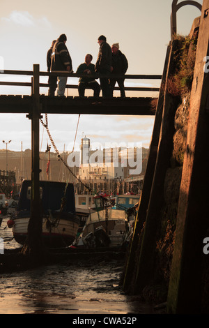 Rassembler les pêcheurs au crépuscule sur une promenade à travers le port de Scarborough à marée basse contre, Scarborough, North Yorkshire, UK Banque D'Images