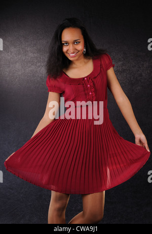 Belle danse et souriante jeune femme en robe rouge sur fond noir Banque D'Images