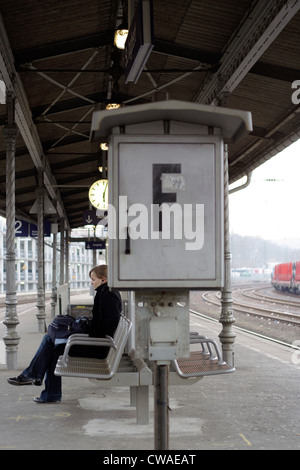 Jeune femme assise sur un banc sur la plate-forme, attendant son train Banque D'Images