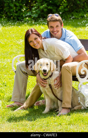 Happy young couple sitting avec golden retriever dog in park Banque D'Images