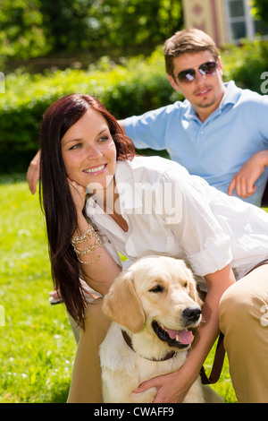 Happy young couple sitting avec golden retriever dog in park Banque D'Images