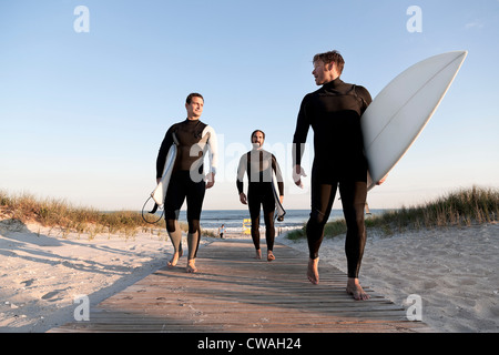 Trois surfeurs marche sur boardwalk Banque D'Images