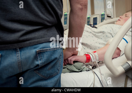 Man holding woman's hand in hospital room Banque D'Images