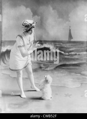 Baigneuse, jeune femme en maillot de bain avec petit chien en face de fond de studio photo, plage, 1913. Banque D'Images