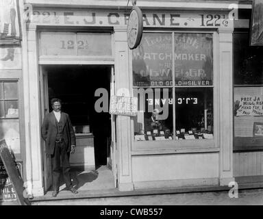 African American horloger, titre original : 'E.J. Crane, horloger et magasin de bijoux avec l'homme et l'homme dans la fenêtre de travail Banque D'Images