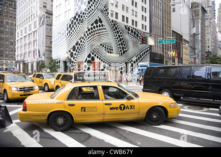 Les gens traversent la 5e Avenue à la 57e rue, avec l'arrêt de l'œil extérieur de la Louis Vuitton flagship store à l'arrière-plan. Banque D'Images