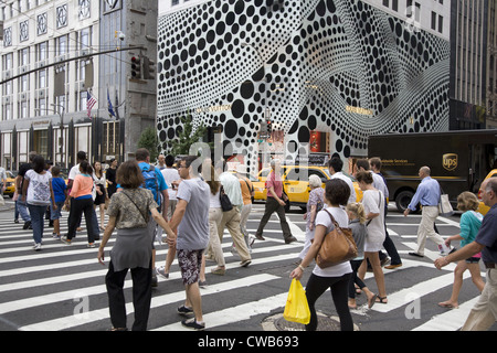 Les gens traversent la 5e Avenue à la 57e rue, avec l'arrêt de l'œil extérieur de la Louis Vuitton flagship store à l'arrière-plan. Banque D'Images