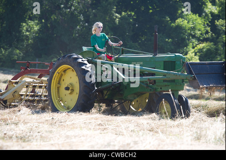 Teenage girl raking hay avec tracteur John Deere modèle 50 et New Holland râteau bar Banque D'Images