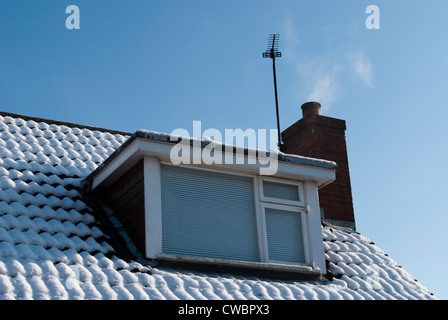 Toit couvert de neige avec lucarne, antenne de télévision et cheminée fumeurs contre sombre ciel bleu Banque D'Images