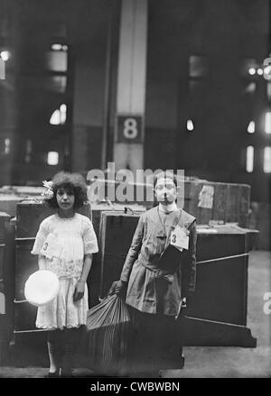 Deux enfants immigrants bien habillé avec le tag 'ERIE' étiquetés à Ellis à l'intérieur des terres, en face d'un grand nombre de lignes de vapeur. Ca. 1910. Banque D'Images