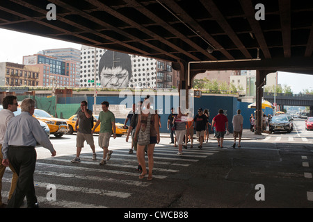 Les visiteurs sous le pont sur chevalets sur 10th Avenue à New York après avoir quitté le parc High Line Banque D'Images