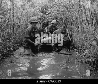 Guerre du Vietnam. Les soldats nous transporter un camarade blessé par une zone marécageuse. 1969. Banque D'Images