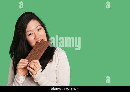 Portrait d'une jeune femme mangeant une grande barre de chocolat sur fond vert Banque D'Images