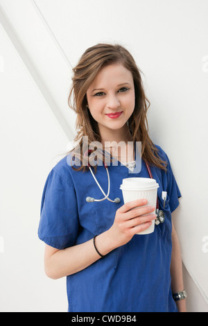 Portrait d'une belle femme médecin tenant un gobelet jetable sur fond coloré Banque D'Images