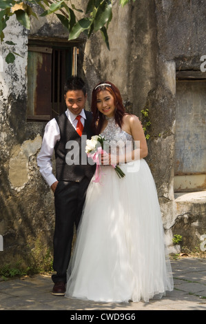 Portrait vertical d'une belle mariée et le marié vietnamienne qui pose pour des photos près d'un bâtiment abandonné au Vietnam. Banque D'Images