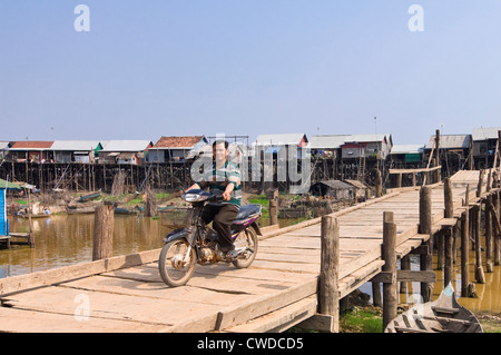 Vue horizontale d'un homme conduisant un cyclomoteur sur un vieux pont de Kompong Khleang village flottant, au Cambodge. Banque D'Images