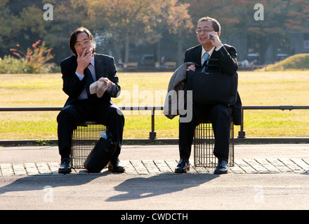 Salarymen japonais se reposant, fumant et parlant sur un téléphone portable dans le parc Hibiya. Tokyo, Japon. Banque D'Images