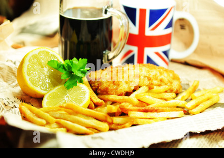 Fish and chips traditionnel avec du citron et de bière brune dans le journal rétractable Banque D'Images