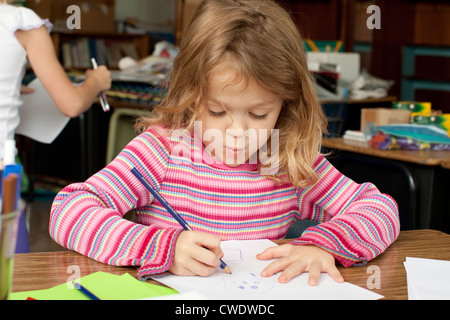 5 ans fille blanche est assis à un bureau et utilise des crayons à dessiner sur feuille de papier Banque D'Images