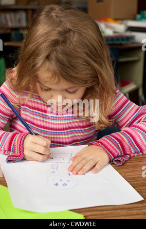 5 ans fille blanche est assis à un bureau et utilise des crayons à dessiner sur feuille de papier Banque D'Images