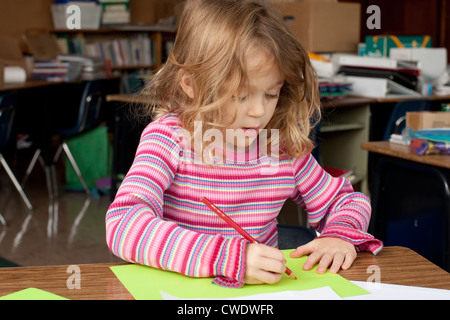 5 ans fille blanche est assis à un bureau et utilise des crayons à dessiner sur feuille de papier Banque D'Images