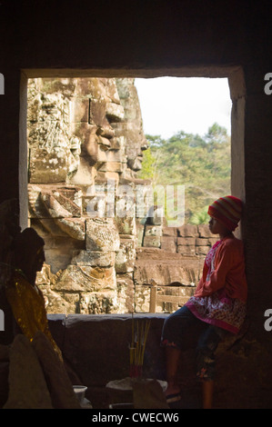 Close up vertical d'un jeune enfant assis cambodgien par une fenêtre le temple Bayon à Siem Reap. Banque D'Images