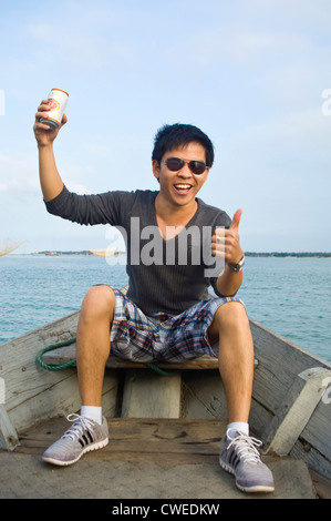 Portrait horizontal d'un jeune homme vietnamien avec un bidon de bière 333, ba-ba-ba de la bière, en disant à la vôtre sur un bateau au soleil. Banque D'Images