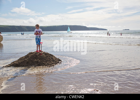 Petit garçon debout sur le dessus de Sandcastle sur plage de Pembrokeshire avec douves 121121 Sand Castle Banque D'Images