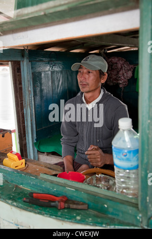 Le Myanmar, Birmanie. Pilote de bateau dans sa cabine, sur la rivière Ayeyarwady près de Mandalay. Banque D'Images