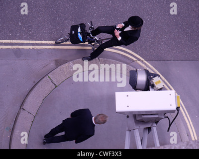 Une caméra de vidéosurveillance surplombe un cycliste portant un chapeau melon dans le centre de Londres, capturant un mélange de style britannique traditionnel, de culture du cyclisme urbain et d'infrastructure moderne de sécurité publique dans les rues de la capitale Banque D'Images