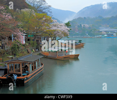 Rivière avec des bateaux traditionnels japonais et fleurs de cerisier avec des collines boisées à l'arrière-plan Banque D'Images