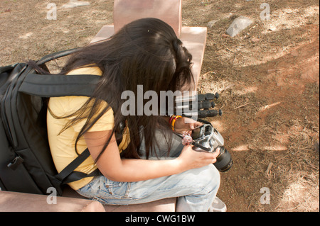 Fille aux cheveux longs l'examen des photos sur un appareil photo numérique peu après de partir en voyage de photographie. Elle porte un sac photo. Banque D'Images