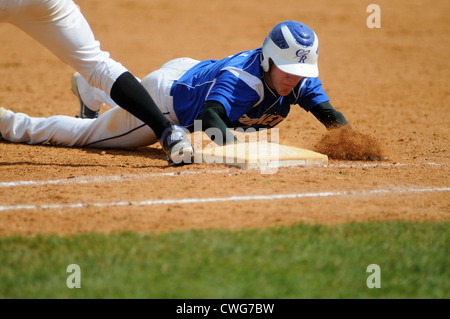 Un coureur de base plonge en toute sécurité de nouveau à la première base pendant un match de baseball à l'école secondaire. ÉTATS-UNIS. Banque D'Images
