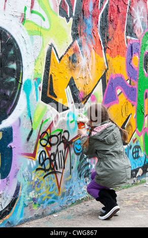 Une jeune fille ajoute sa note au dessus d'autres graffitis sur une partie du mur de Berlin, Berlin, Allemagne. Banque D'Images