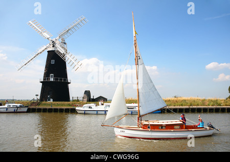 Un petit voilier sur la rivière Yare à Norfolk, en Angleterre, avec d'autres bateaux et le moulin à vent restauré Berney Armoiries derrière Banque D'Images