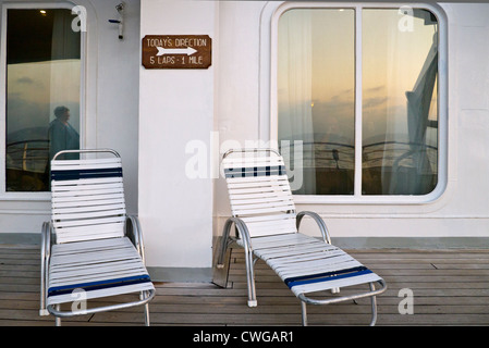 Chaises vides sur le pont d'un navire de croisière, un avis encourageant l'exercice (5 tours, 1 mile), une réflexion du passager, coucher du soleil Banque D'Images