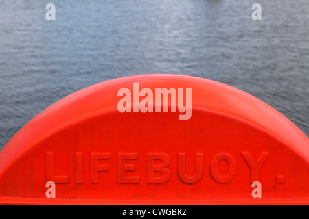 Rouge orange vif contenant bouée en plastique sur le bord de mer avec une mer calme derrière. L'équipement de sécurité, de couleurs vives, Cornwall, UK Banque D'Images